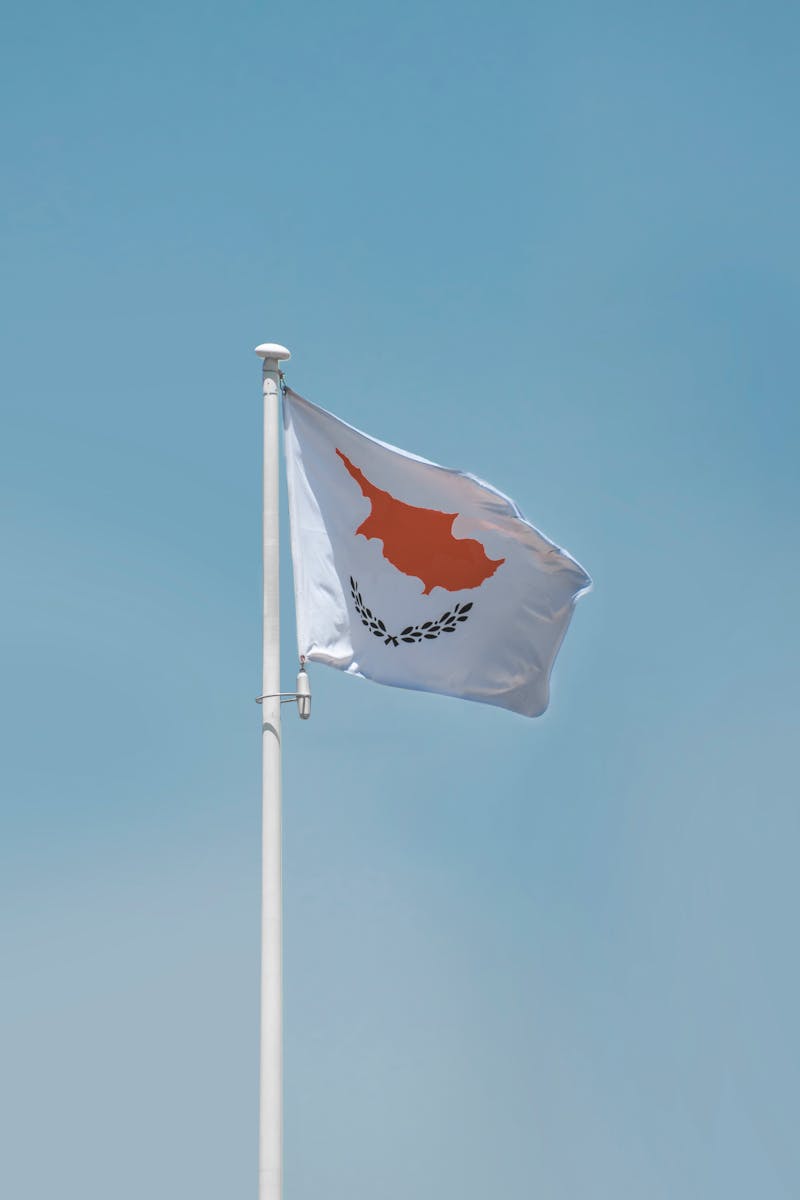 The Cyprus national flag waving on a flagpole against a clear blue sky, showcasing patriotism.