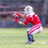 A football player in red uniform dramatically catching a ball on a grassy field during a game.
