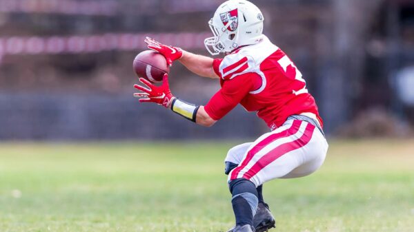 A football player in red uniform dramatically catching a ball on a grassy field during a game.