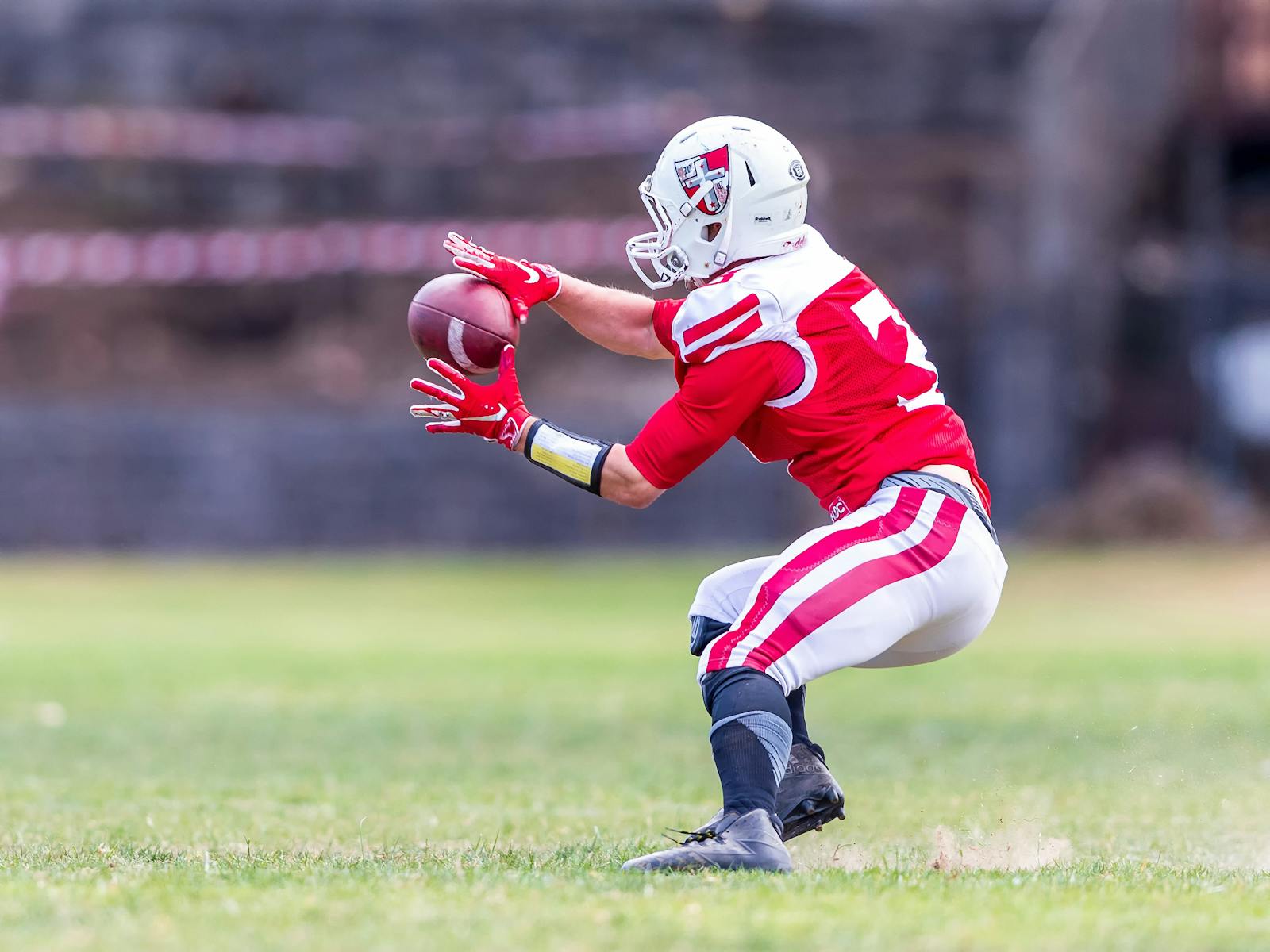 A football player in red uniform dramatically catching a ball on a grassy field during a game.
