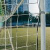A close-up of a soccer goal and net on an urban pitch with city buildings in the background.