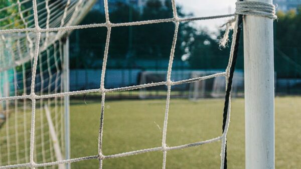 A close-up of a soccer goal and net on an urban pitch with city buildings in the background.