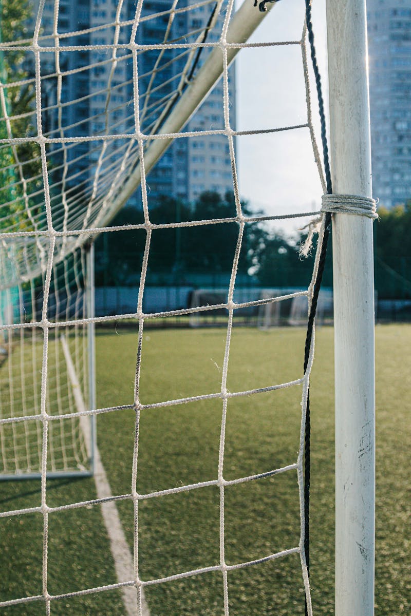 A close-up of a soccer goal and net on an urban pitch with city buildings in the background.