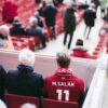 Fans in red jerseys sit in a stadium, showcasing football spirit with vibrant energy.