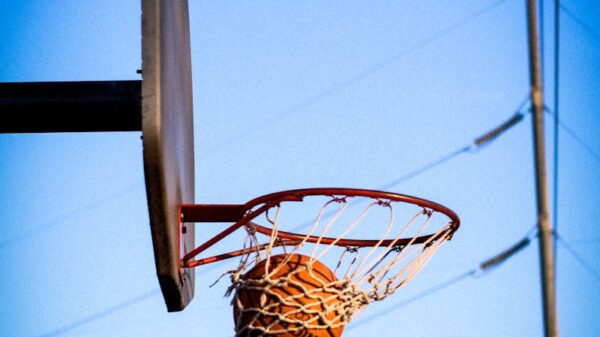 A basketball perfectly swishes through the hoop on an outdoor court against a clear blue sky.