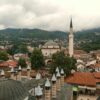 Aerial view of Sarajevo's historic rooftops and minarets with lush mountains in the background.