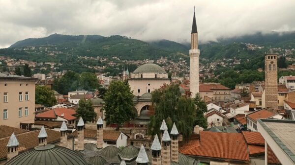 Aerial view of Sarajevo's historic rooftops and minarets with lush mountains in the background.