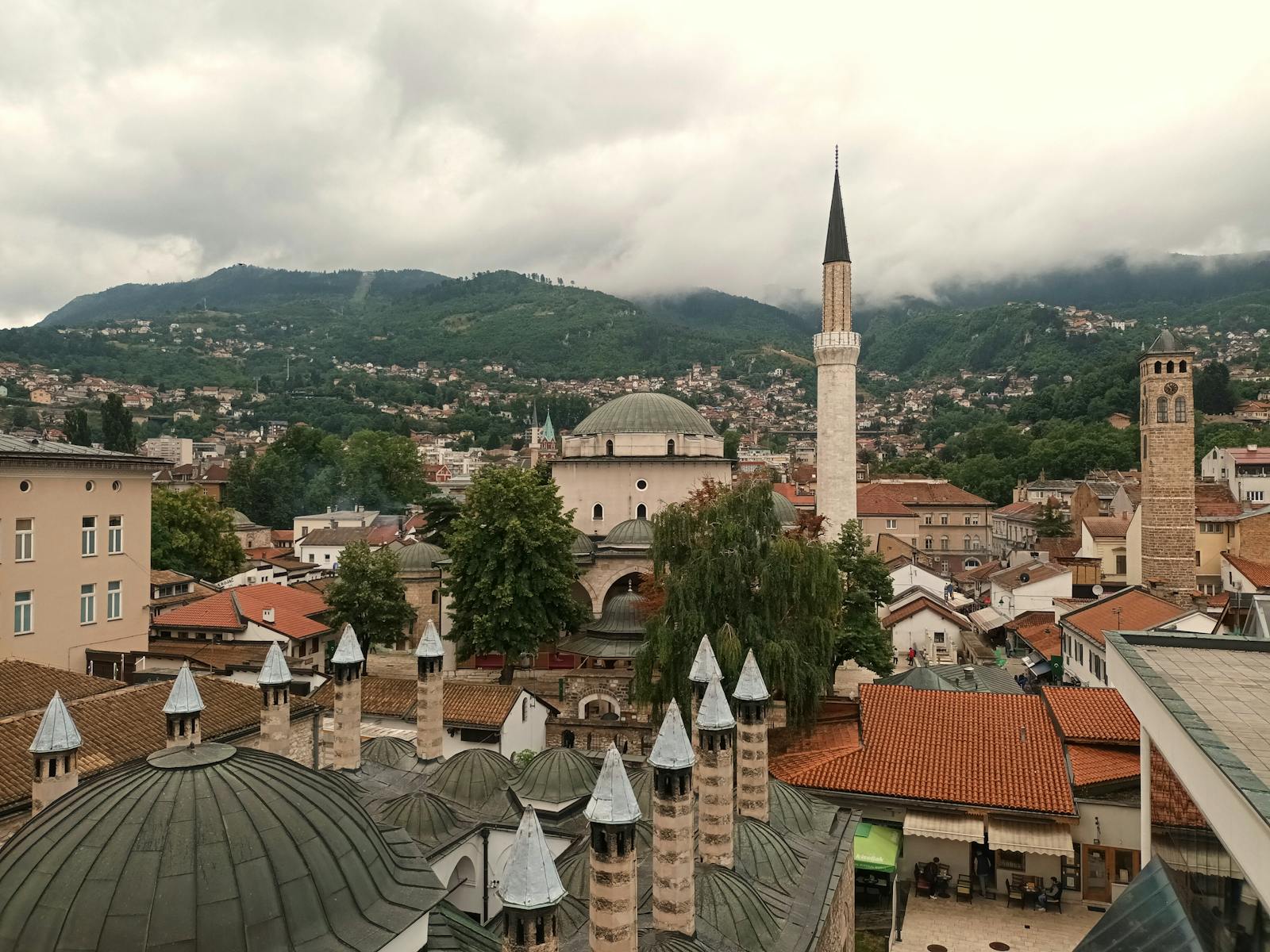 Aerial view of Sarajevo's historic rooftops and minarets with lush mountains in the background.