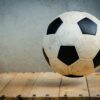 Vintage soccer ball resting on wooden planks against a textured background, symbolizing sports tradition.
