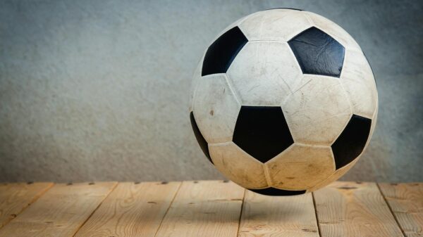 Vintage soccer ball resting on wooden planks against a textured background, symbolizing sports tradition.