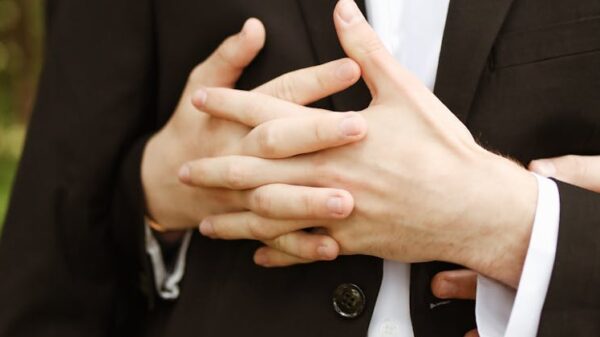 Two men in formal suits embrace lovingly in an outdoor setting.