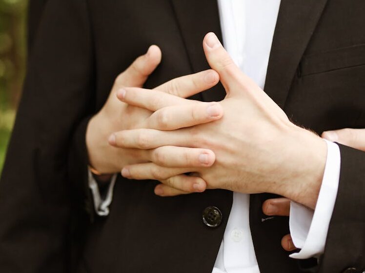 Two men in formal suits embrace lovingly in an outdoor setting.
