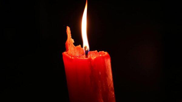 Close-up of a burning red candle glowing in the dark, symbolizing warmth and hope.
