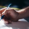 Detailed shot of a hand holding a blue pen while signing a document. Ideal for legal and business themes.