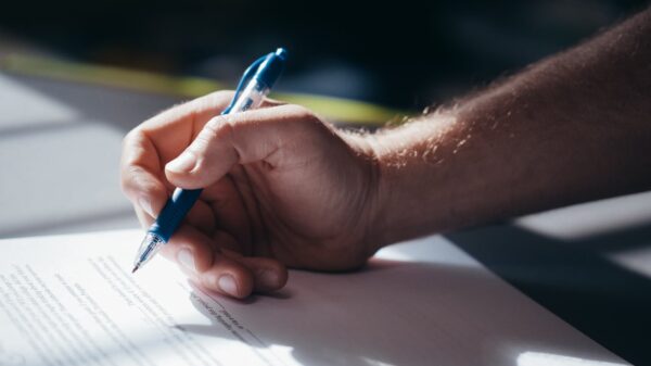 Detailed shot of a hand holding a blue pen while signing a document. Ideal for legal and business themes.