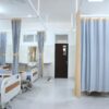 Spacious hospital ward in Surabaya, Indonesia with multiple medical beds and privacy curtains.