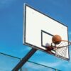A basketball scoring shot on an outdoor court with a clear blue sky backdrop.