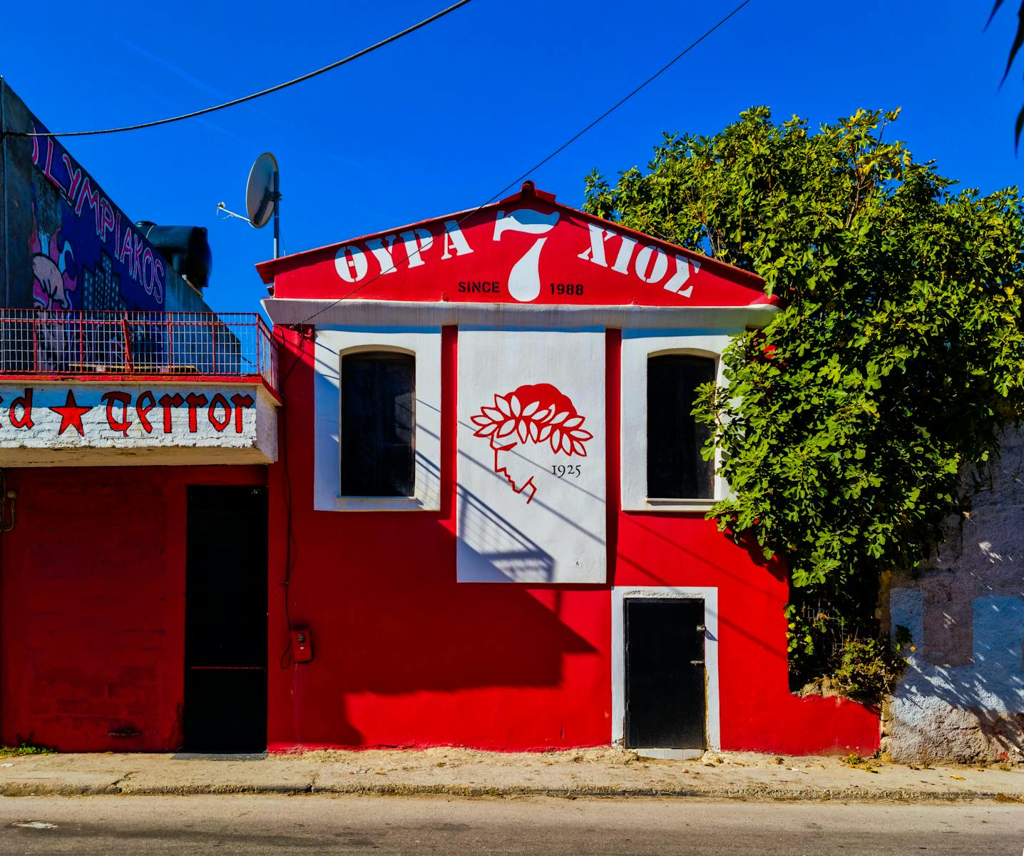 Colorful urban building in Chios with red facade and artistic mural under blue sky.