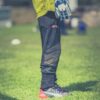 Goalkeeper standing on green field, focused on legs with gear, during a sunny day soccer match.