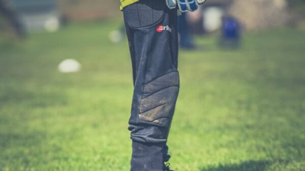 Goalkeeper standing on green field, focused on legs with gear, during a sunny day soccer match.