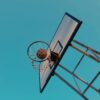 Low angle shot of basketball swishing through a hoop against a clear blue sky.