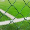 Close-up of a green metal wire fence with grass field in the background.
