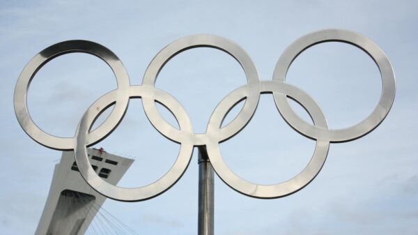 The iconic Olympic rings in front of a tall structure on a clear day.