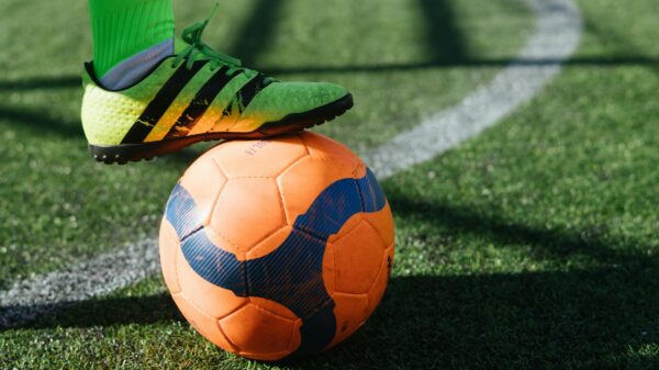 Dynamic shot of a soccer player's foot on a vivid orange ball on a lush green field.