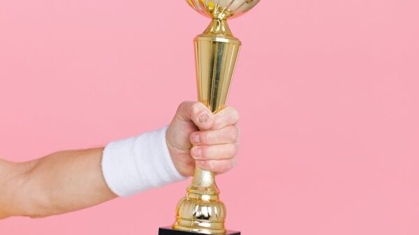A hand holding a golden trophy against a vibrant pink background, symbolizing victory and success.