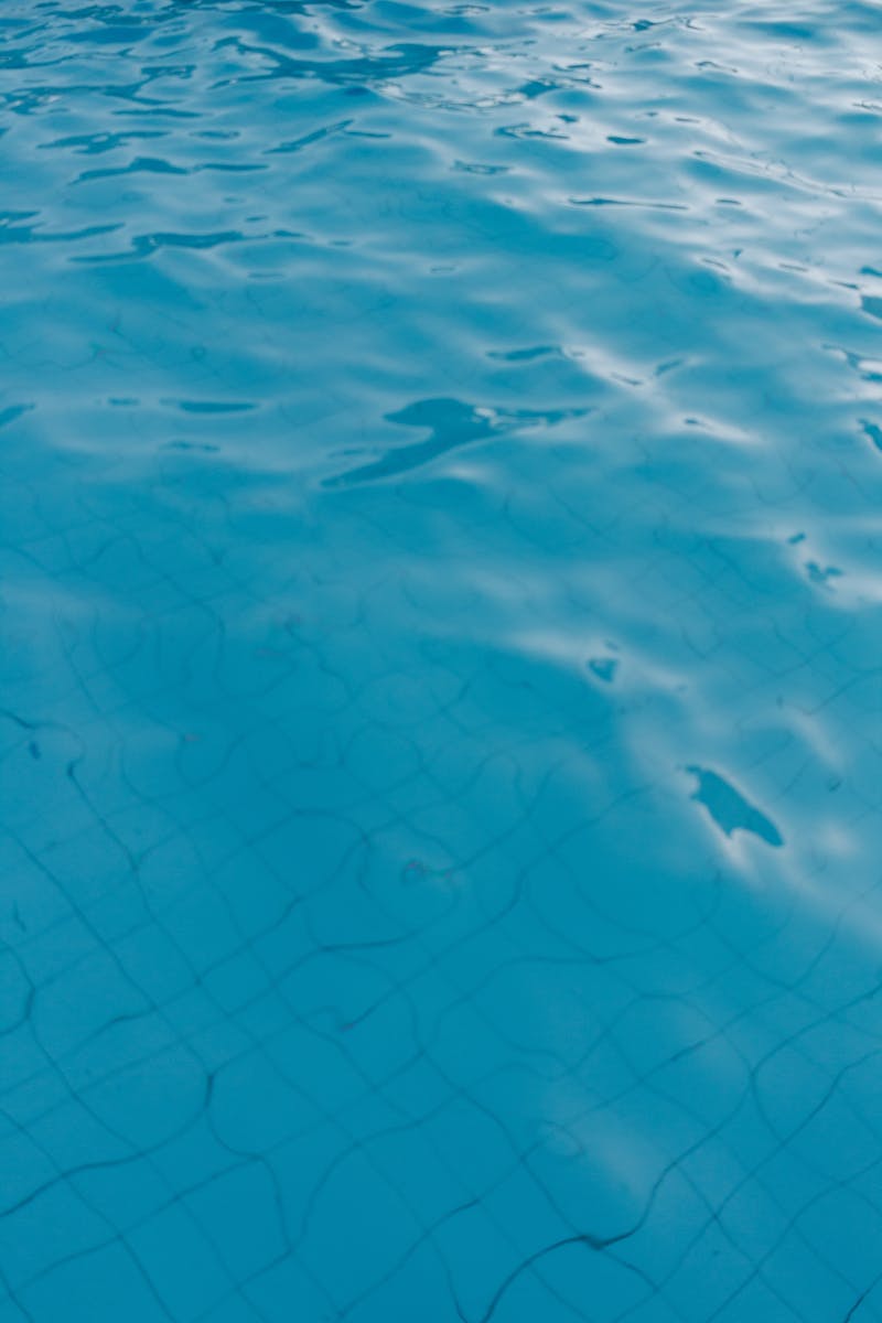 Close-up of a vibrant blue swimming pool surface with gentle ripples and tile lines visible underwater.
