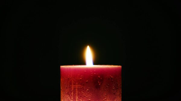 A solitary red candle with a bright flame against a dark background, creating a serene atmosphere.