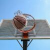 A low-angle shot of a basketball making its way through the hoop against a clear blue sky.