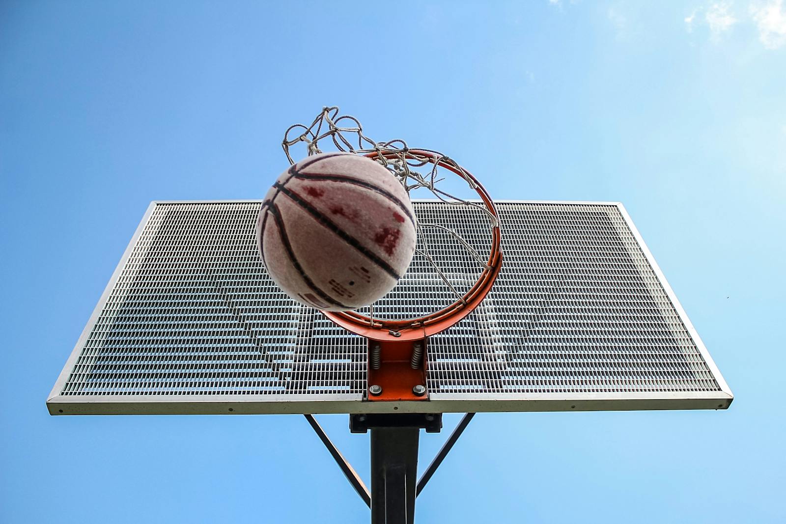 A low-angle shot of a basketball making its way through the hoop against a clear blue sky.