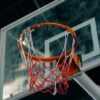 Old basketball hoop with frayed net on outdoor court, viewed from below.