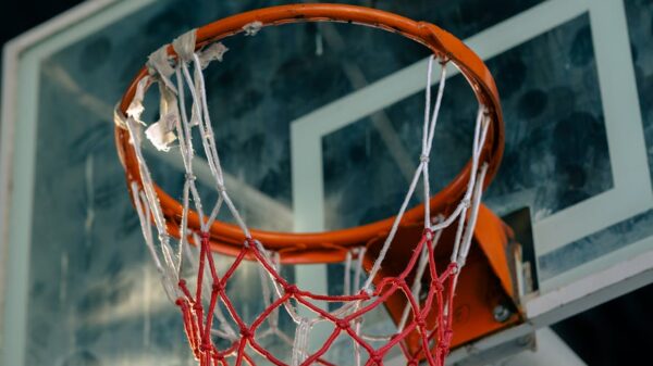 Old basketball hoop with frayed net on outdoor court, viewed from below.