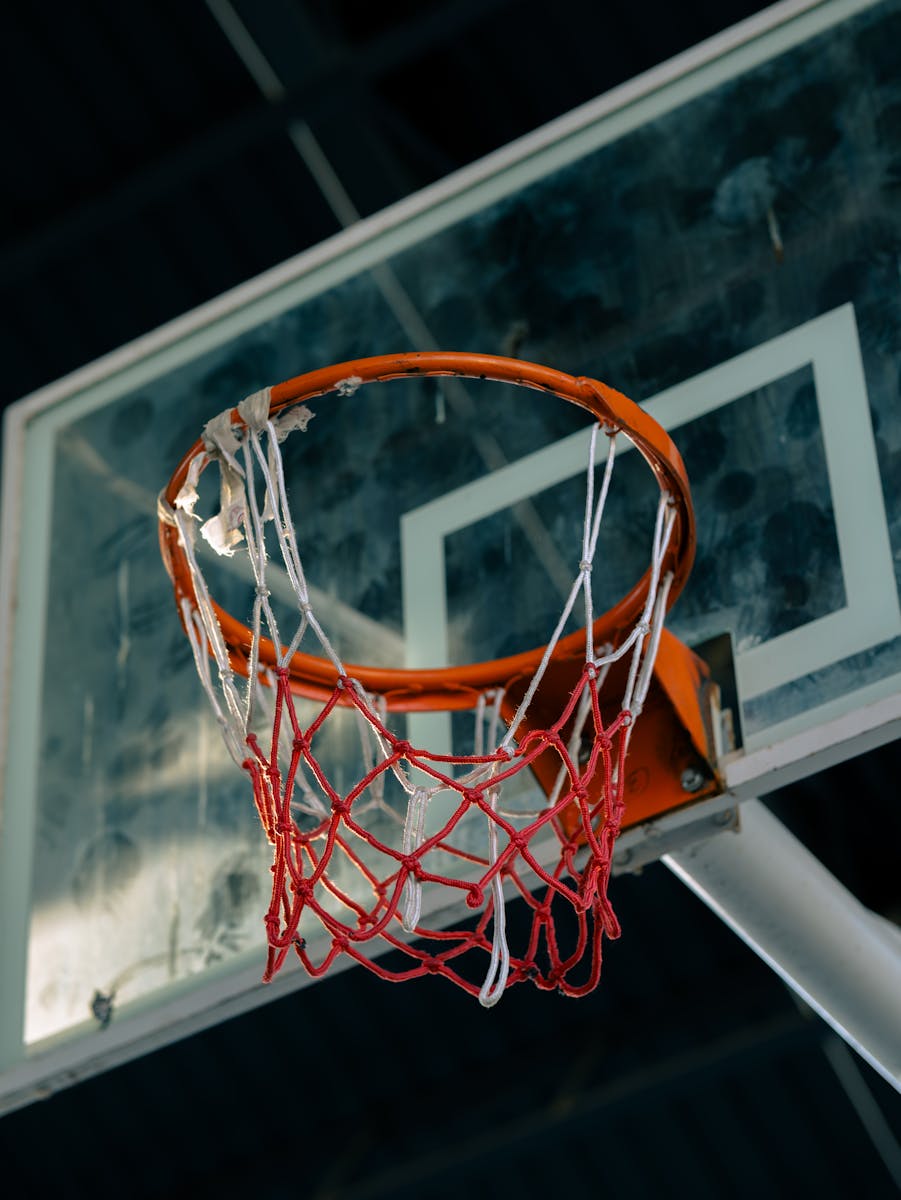 Old basketball hoop with frayed net on outdoor court, viewed from below.