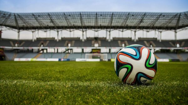 Close-up of a soccer ball on a lush grass field with an empty stadium in the background.
