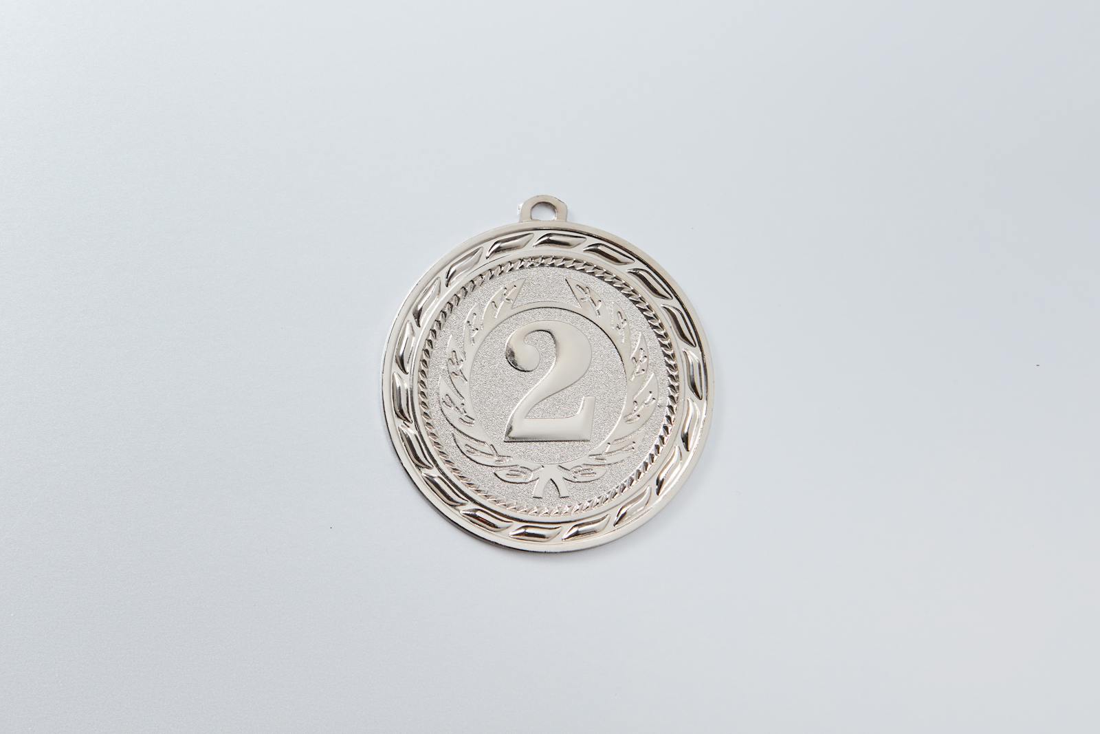 Close-up of a silver second place medal with an engraved number 2 on white background.