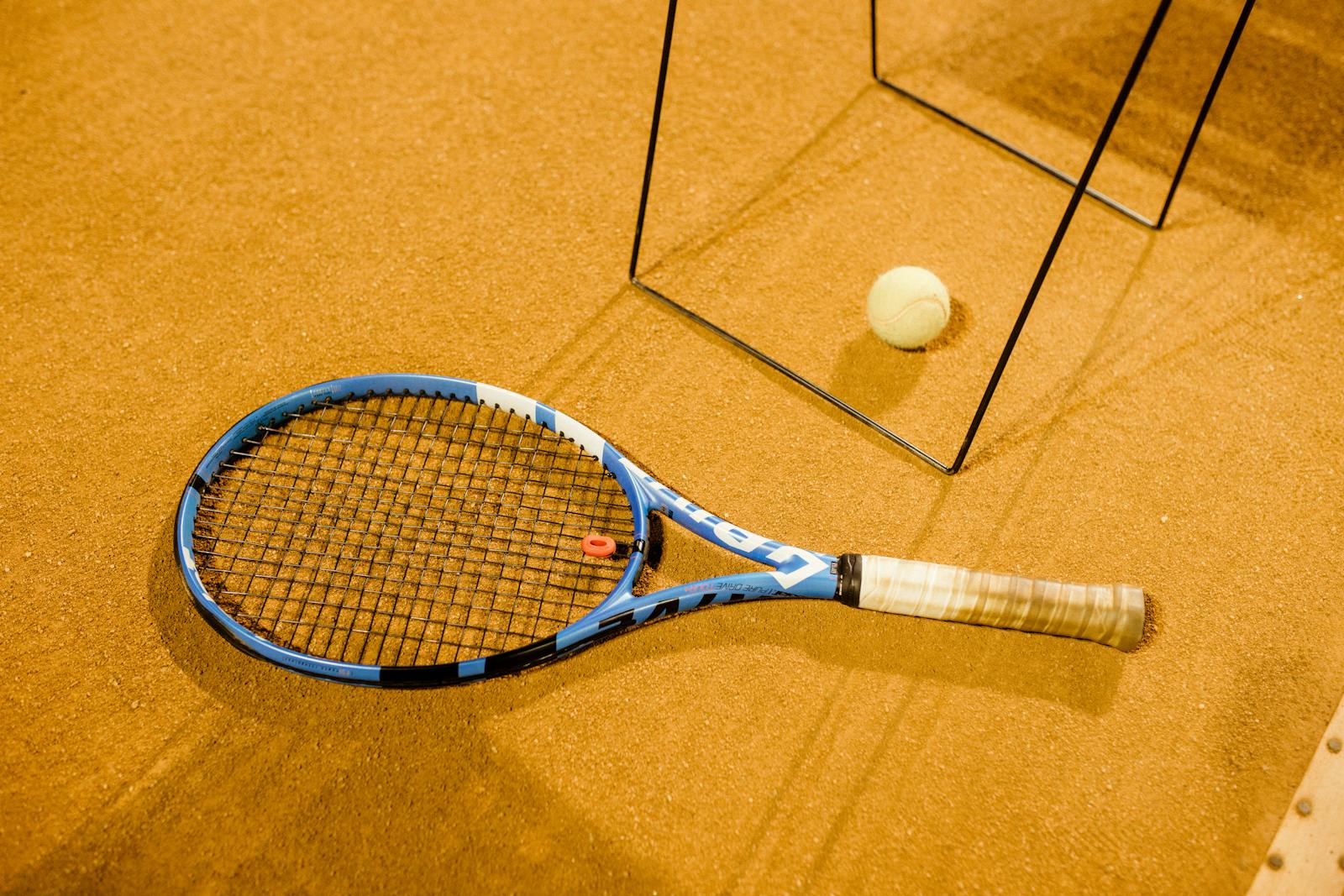 Close-up of a blue tennis racket and ball on an indoor clay court, perfect for sports imagery.