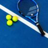 Tennis racket and three balls on a vibrant blue court.
