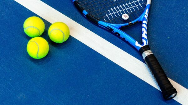 Tennis racket and three balls on a vibrant blue court.
