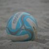 A close-up of a colorful beach volleyball resting on sand.