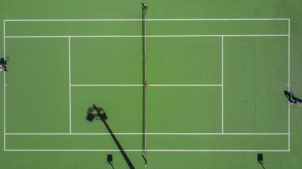 High-angle drone shot of a tennis match on a bright green court with shadows.