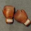 Brown leather boxing gloves on a textured gray gym surface.