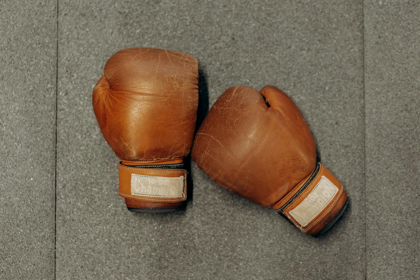 Brown leather boxing gloves on a textured gray gym surface.