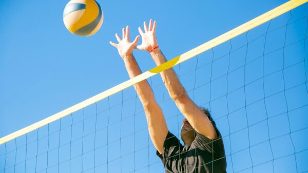 Dynamic outdoor volleyball game with a male player blocking a ball under clear blue skies.