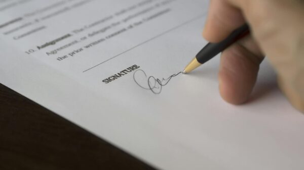 A hand signs a formal contract with a pen on a wooden desk.