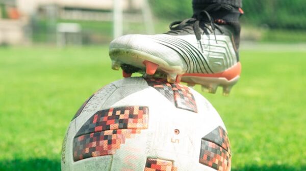 Close-up of a soccer ball with a player's foot on it, set on a vibrant green soccer field during a sunny day.