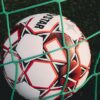 Close-up of a soccer ball trapped in a net on a grassy pitch, perfect for sports themes.