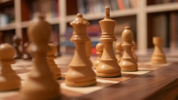 Close-up of wooden chess pieces on a chessboard in a warm, cozy library setting.